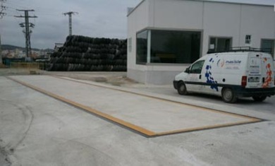 Báscula industrial instalada junto a un edificio y una camioneta de empresa estacionada cerca, utilizada para el pesaje de vehículos de transporte